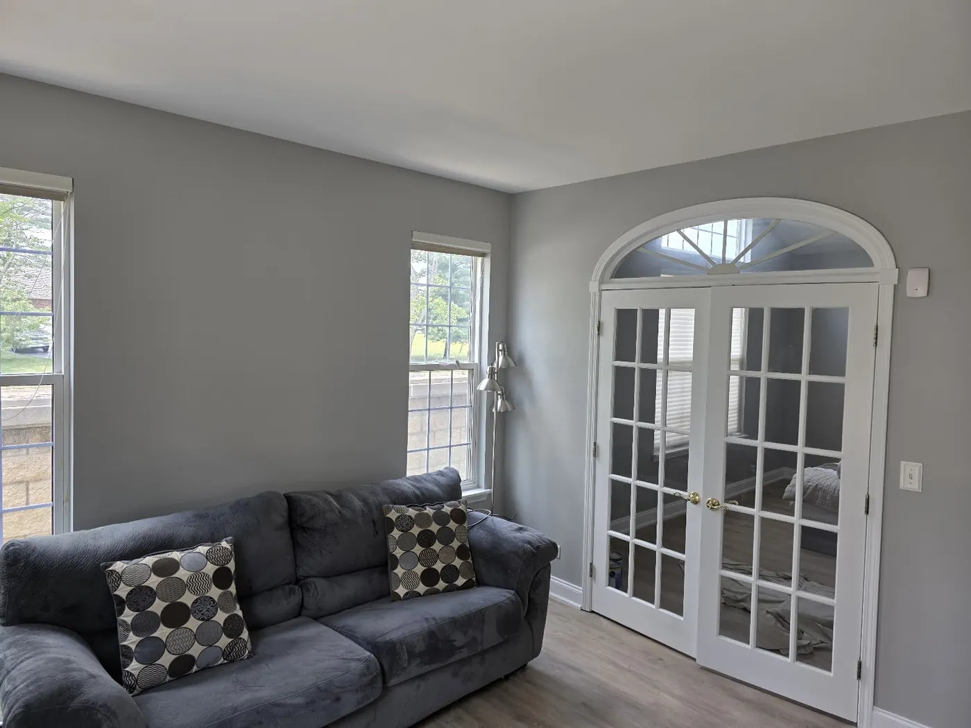 Living room with freshly painted grey walls, white trim and arched French doors.